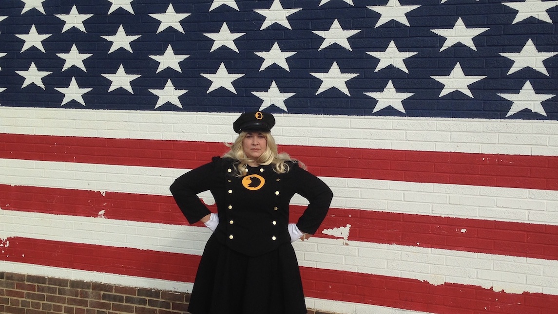 Nancy Brown poses in front of American Flag in Lady Blackhawk costume.